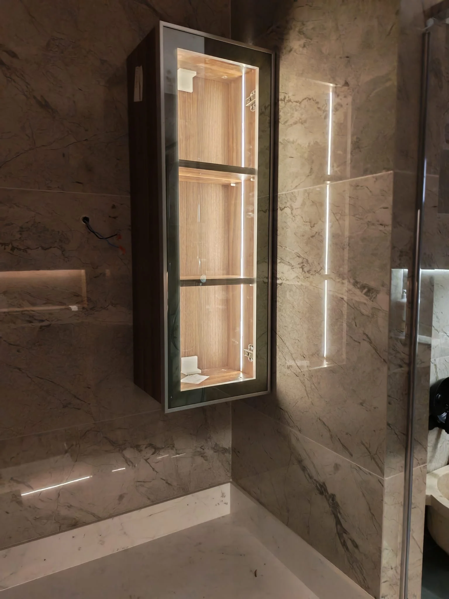 Taş desenli duvarlar, cam duş bölmesi ve aydınlatılmış dikey niş bulunan banyo