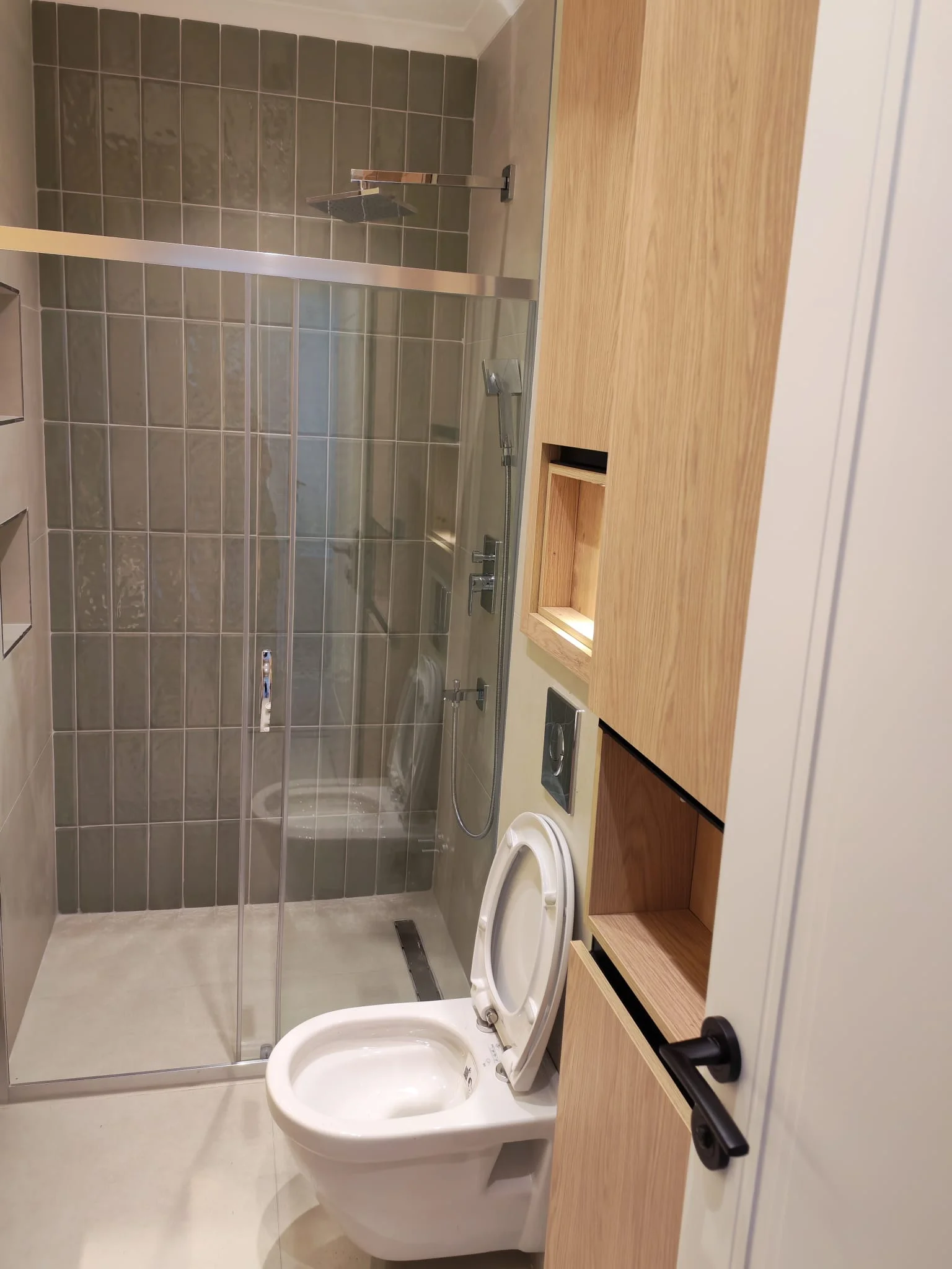 Cam duş bölmesi, klozet ve ahşap kapaklı çamaşır makinesi dolabı bulunan banyo