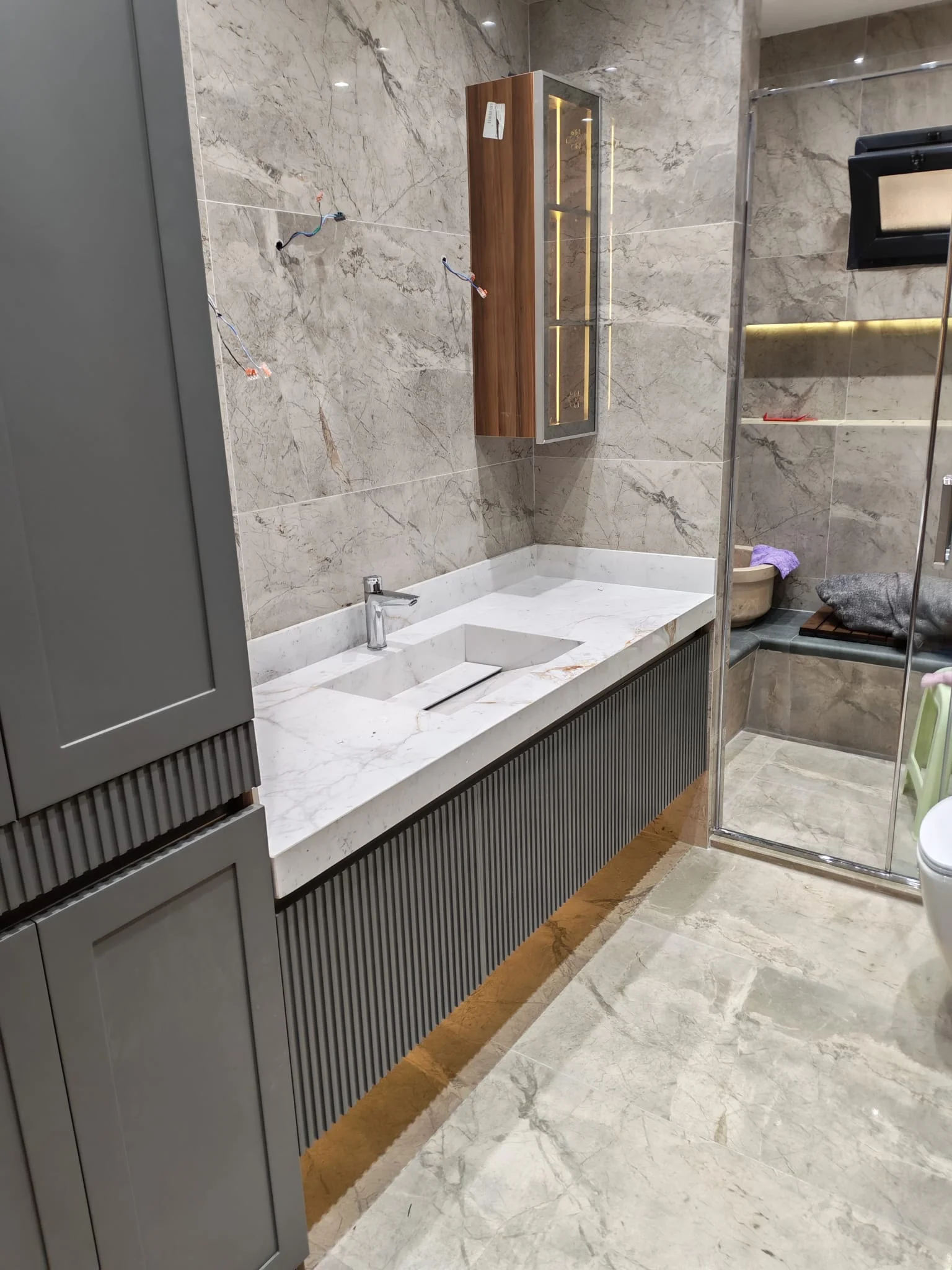 Taş desenli duvar, geniş ayna ve ahşap tonlu lavabo dolabı bulunan banyo